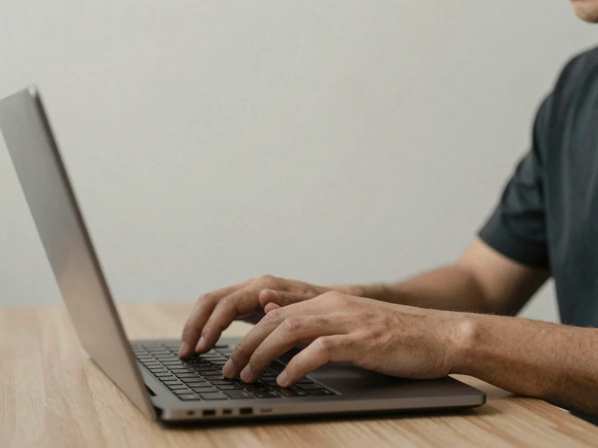 Medium shot of a person typing on a laptop with a clean architectural background, focus on hands and keyboard, soft natu